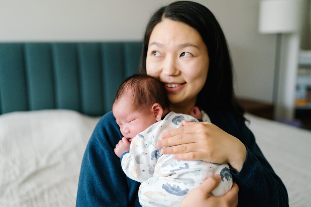 Outfit inspiration for newborn photoshoot, Mother in blue holding baby boy in lightly printed sleeper for Seattle in home newborn photo session