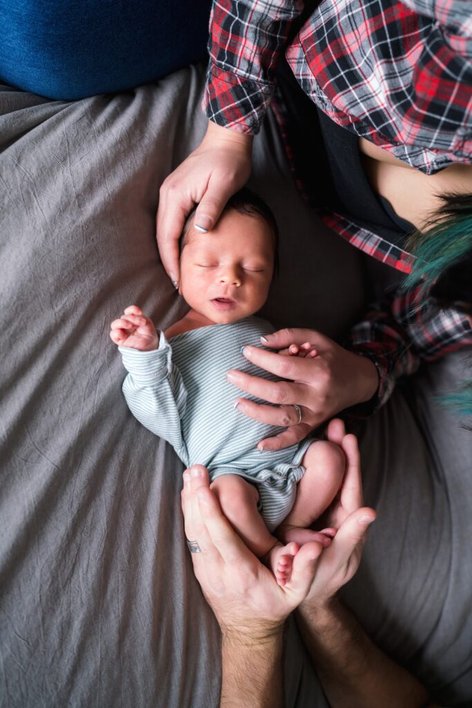 Newborn baby with parents offering comfort, choose a newborn photographer tips