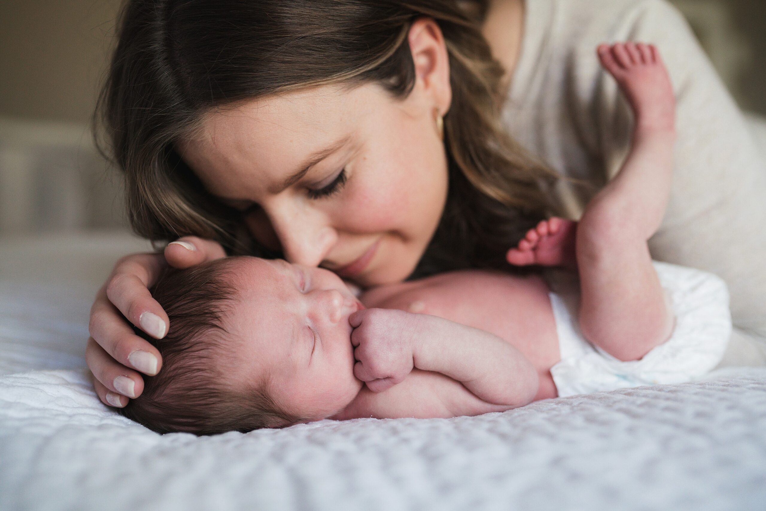 Mother nuzzling newborn baby girl in a diaper on master bed during a Snoqualmie Valley relaxed newborn photography session