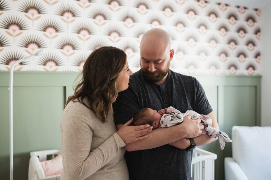 Parents snuggling newborn baby in a gorgeous green and floral nursery