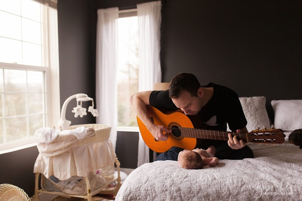 father playing guitar for newborn baby during in home newborn photography session