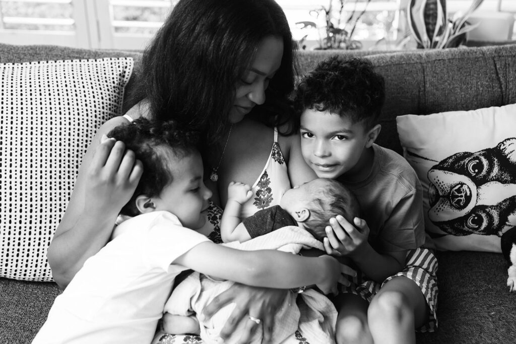 black and white photo of mother with newborn baby and two boys during in home newborn photography session in the greater Seattle area
